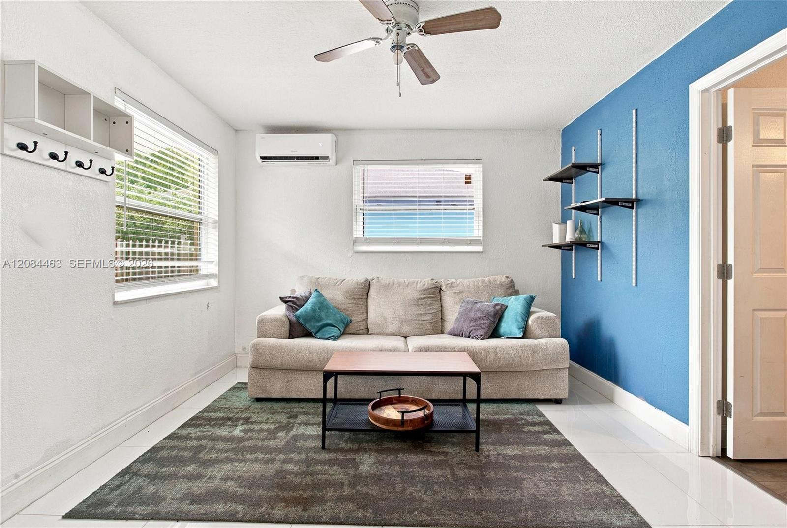 Cozy, fully furnished living area featuring a comfortable sofa, coffee table, wall-mounted TV, and decorative shelving. A bright, inviting, move-in-ready space