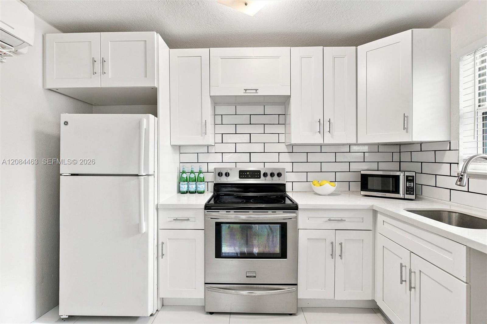 Updated kitchen featuring white cabinetry, subway-tile backsplash, generous counter space, modern appliances, and abundant natural light.