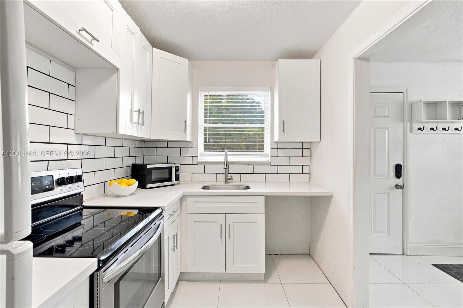 Updated kitchen featuring white cabinetry, subway-tile backsplash, generous counter space, modern appliances, and abundant natural light.