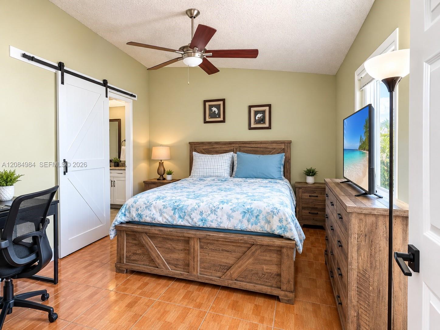 Spacious bedroom featuring wood-look ceramic tile flooring, ceiling fan, and barn door detail.