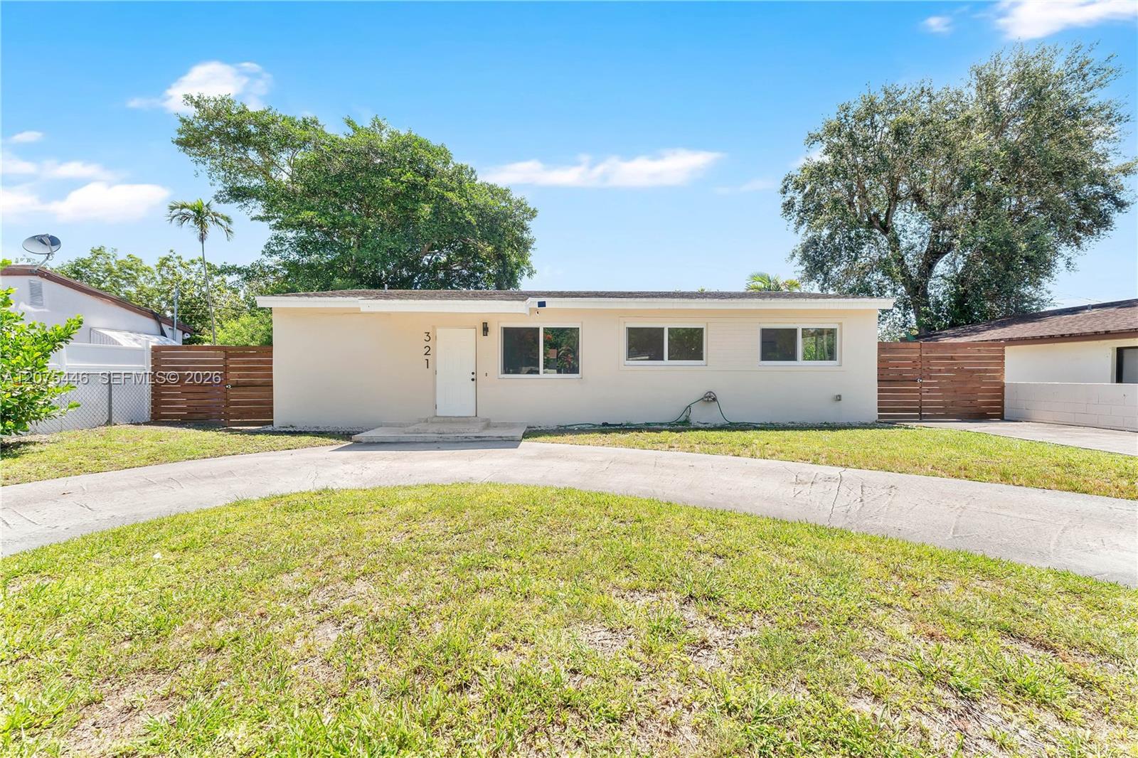 Clean mid-century ranch-style home with fresh white exterior, modern horizontal wood privacy fencing, and a spacious corner lot with lush green lawn.