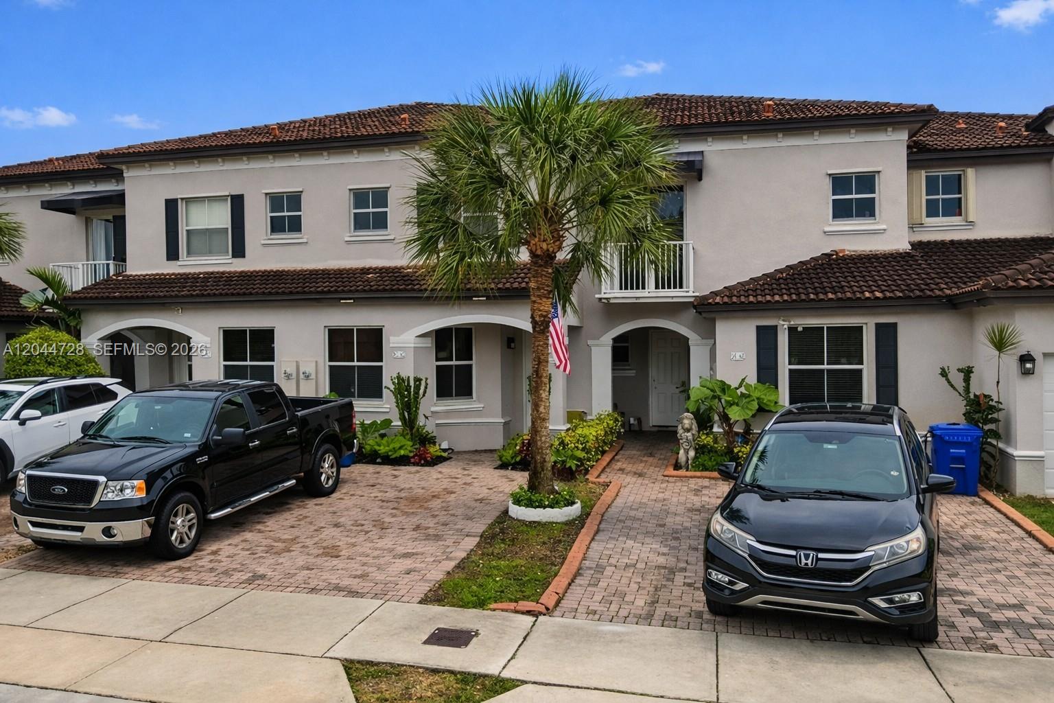 Two-story residence with a clean exterior and a lovely front entry. Features a tiled roof, white-framed windows, and a tropical garden with tall succulents and ornamental plants. Located in the desirable Century Gardens condominium.