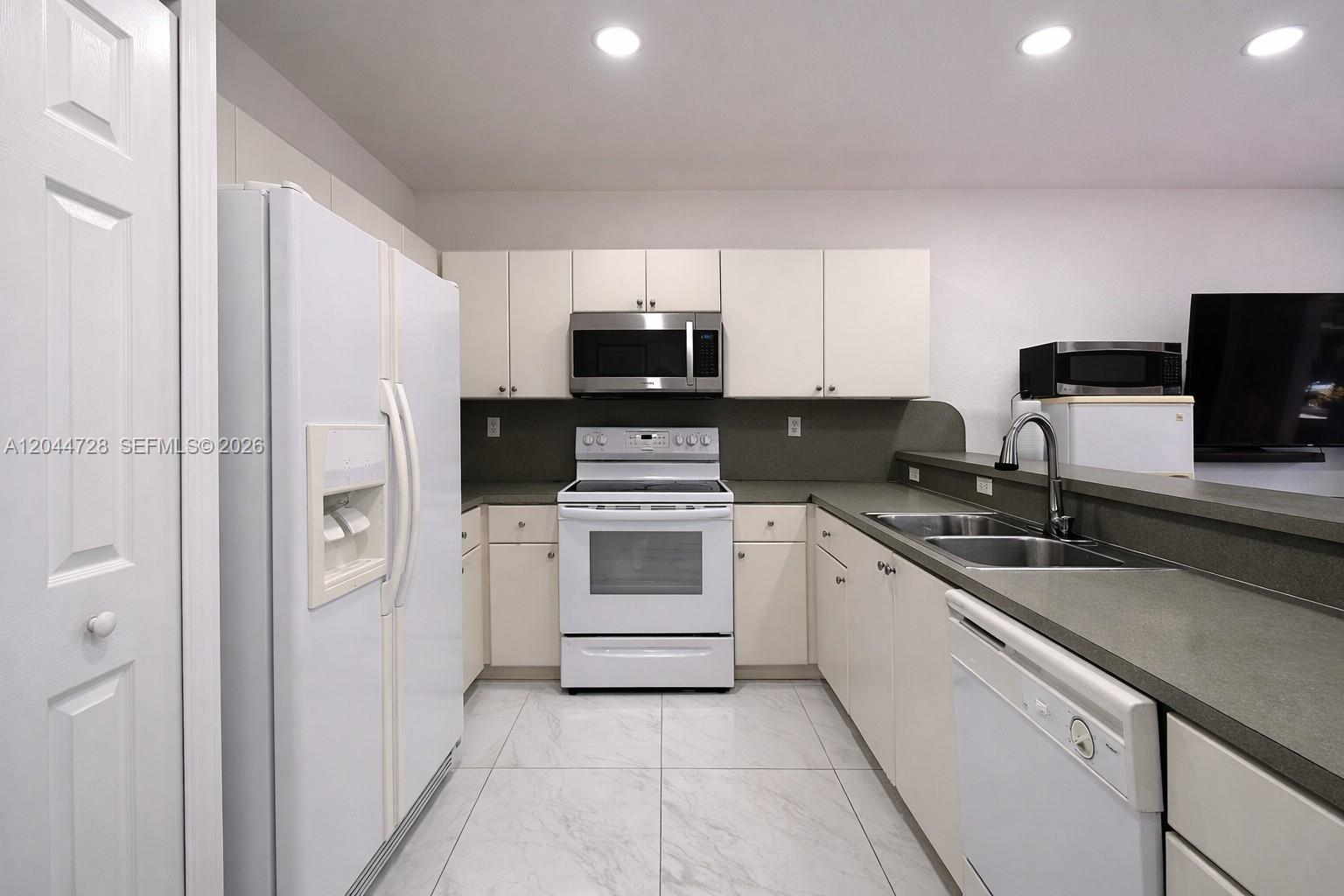 Bright and clean kitchen with white cabinetry, and spacious tile flooring. Functional layout with ample counter space and a fresh, well-maintained look.