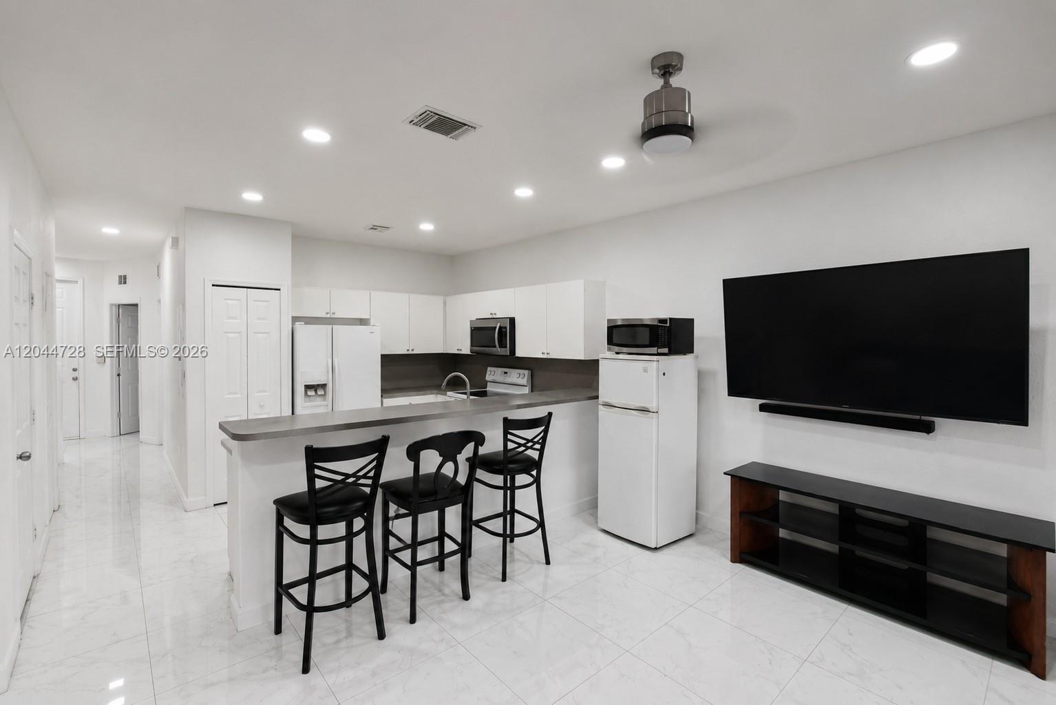 Bright open kitchen and living area with white appliances, and clean tile flooring. Clean, functional layout with a contemporary feel.