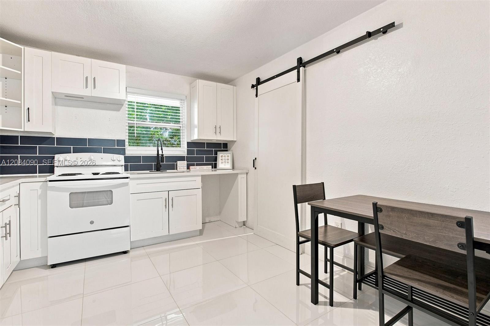 Bright eat-in kitchen with white cabinetry, modern backsplash, ample counter space, and a stylish barn door leading to the laundry area.