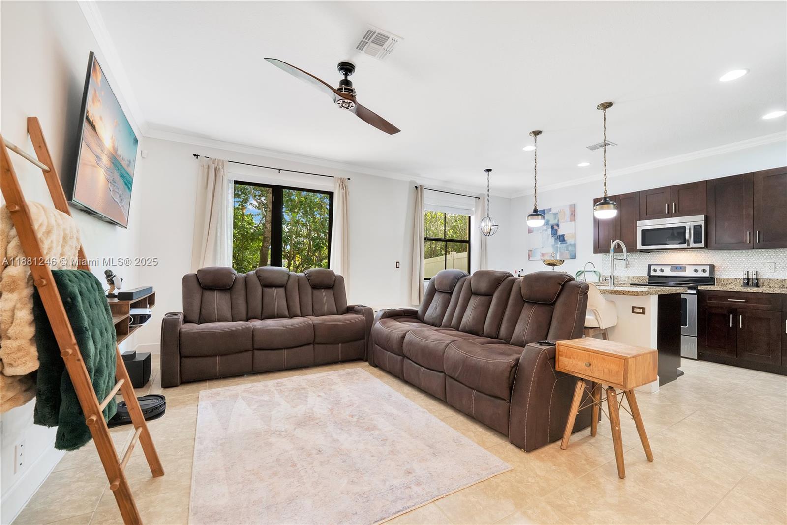 Bright open-concept living with reclining sofas and seamless kitchen access featuring granite and stainless steel.