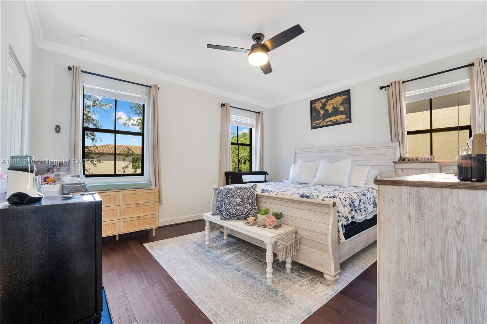 Spacious primary bedroom with large windows, ample natural light, and a modern ceiling fan. Features a light wood furniture set and a cozy, inviting atmosphere.